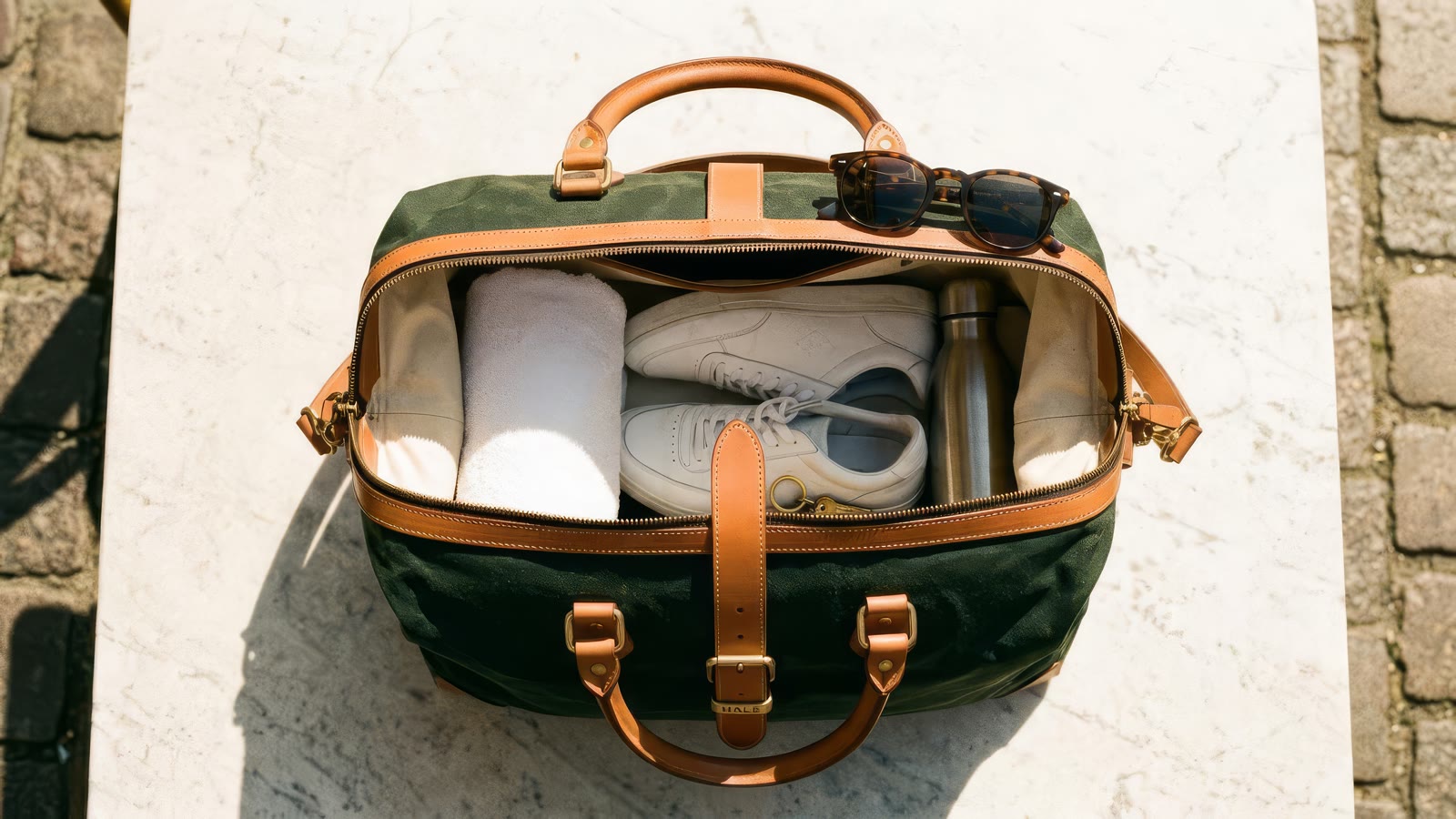 The holdall from above, zip open, packed with a towel, sneakers, a steel bottle and sunglasses