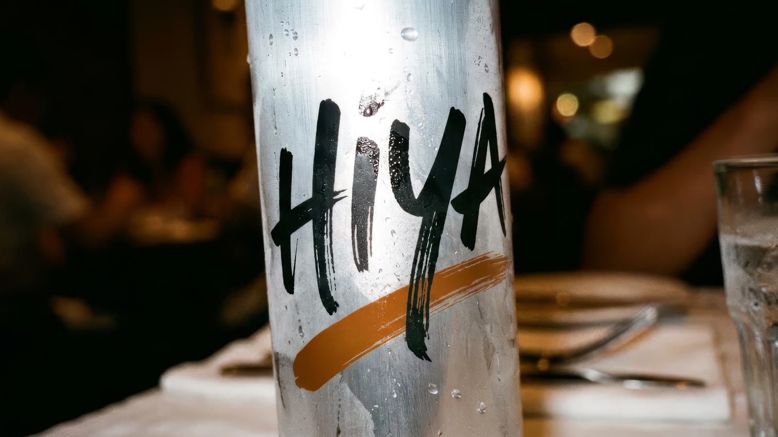 Macro of black brush lettering reading HiYA and a burnt amber stroke on a cold wet can