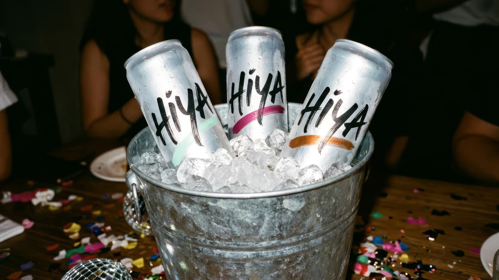 Three HIYA cans pushed into a steel bucket of crushed ice at a house party with confetti